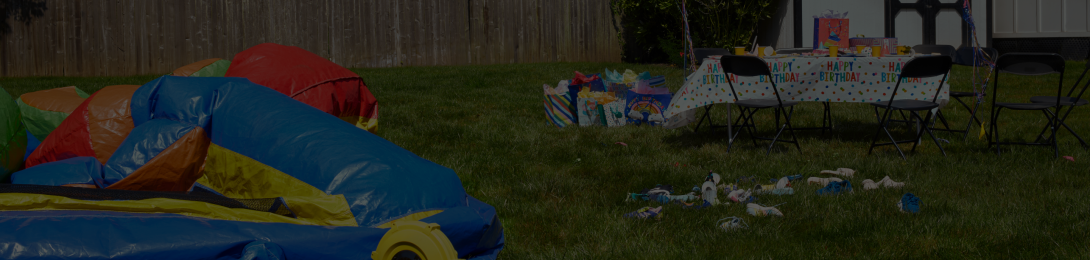 A chaotic birthday party scene, with an uninflated bouncy castle and party debris on the grass.