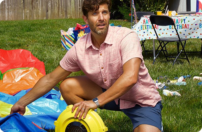 A man has a panicked expression while struggling to inflate a bouncy house.