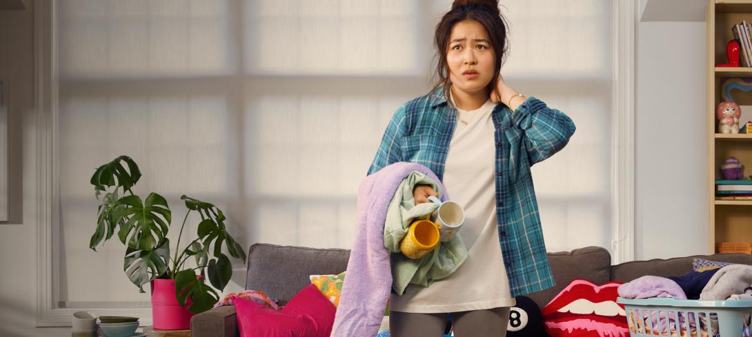 An anxious-looking young woman holds a basket of unfolded laundry.