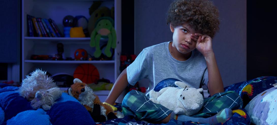 A young boy rubs his eyes, struggling to sleep through the night.