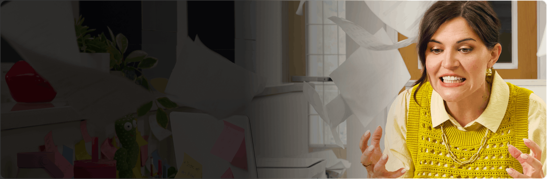 A woman grits her teeth in frustration as office papers fly around her desk.