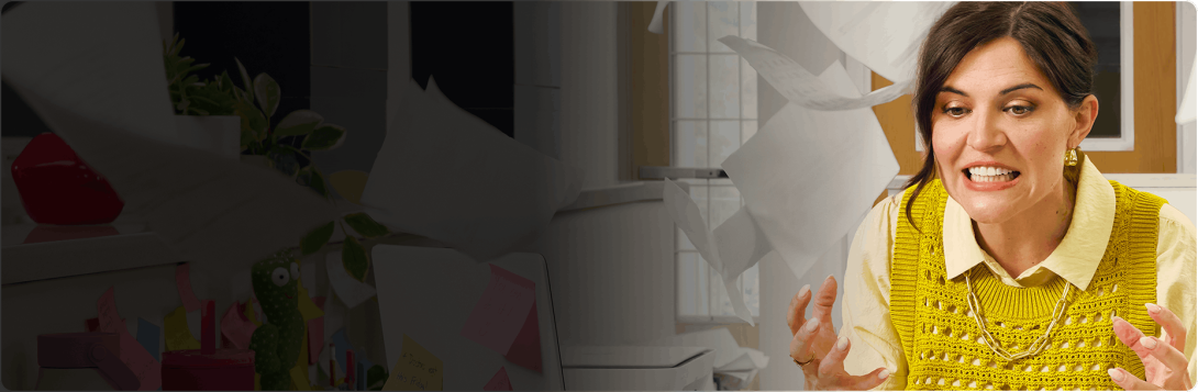 A woman grits her teeth in frustration as office papers fly around her desk.